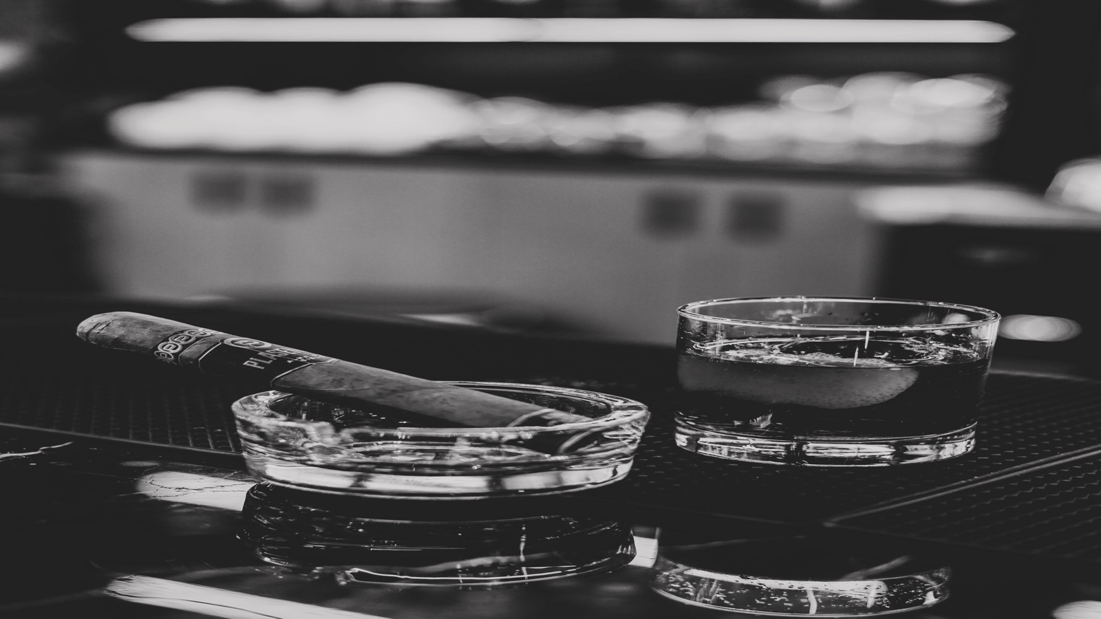 A cigar resting in a glass ashtray beside a whisky glass